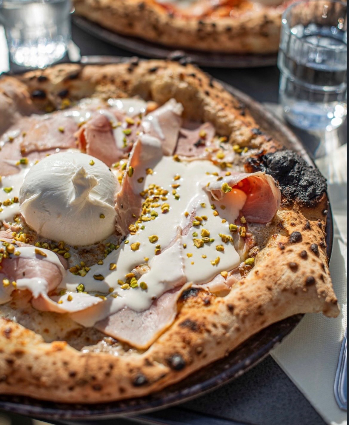 Une pizza napolitaine dorée sortant du four traditionnel, garnie de tomates, mozzarella et basilic frais.